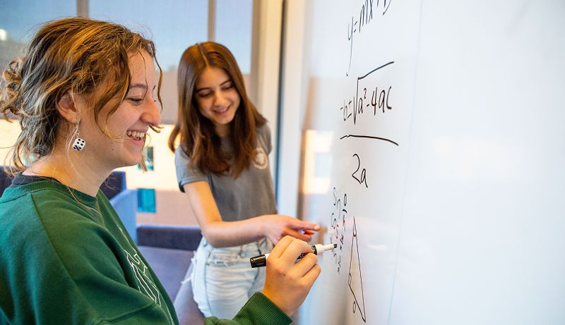 Two smiling girls do math on a whiteboard