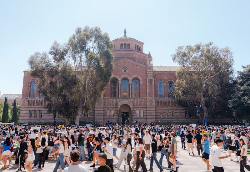 A large crowd of UCLA students gathers for an outdoor activities fair in front of Royce Hall, exploring student organizations and campus resources.