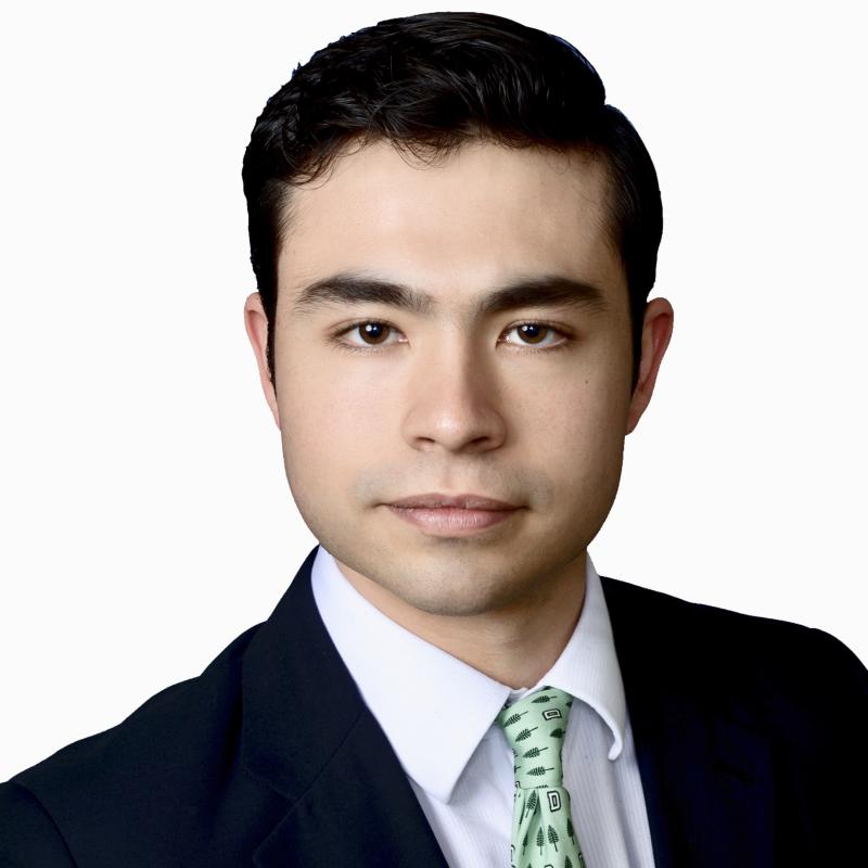 Picture of white man with black combed hair wearing a black suite, white shirt, and green patterned tie on a white background