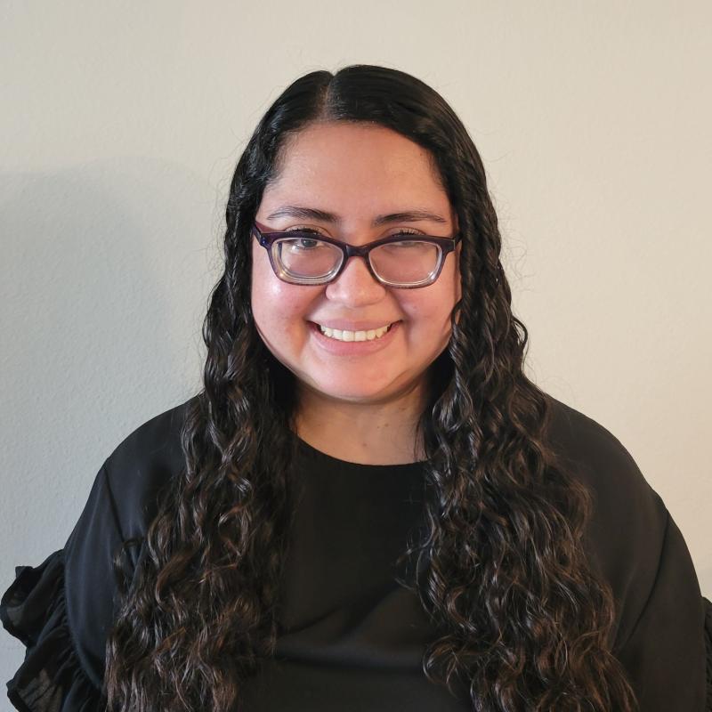 Picture of a smiling Latina woman in a black blouse wearing black glasses