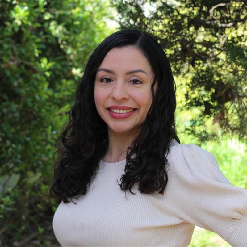 Photo of woman with long black hair smiling and wearing a white blouse